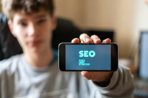 young male worker holding a smartphone with SEO text design in the office, search engine